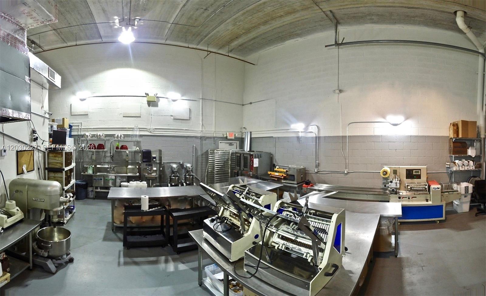 A commercial kitchen features stainless steel prep tables, industrial mixers, and various food processing equipment — 1365 NW 98th Ct, Doral FL 33172, DORAL, FL