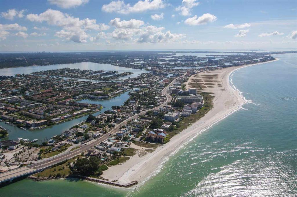 An aerial view shows a coastal town with a long sandy beach and residential buildings — 11605 GULF BOULEVARD UNIT 506, TREASURE ISLAND, FL