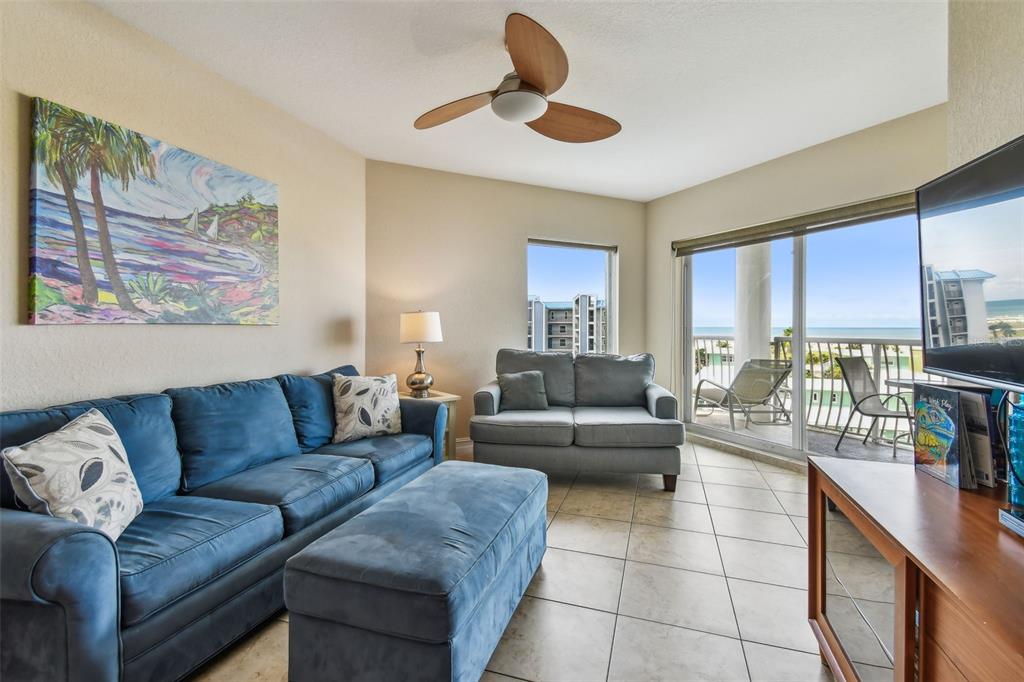 A living room features a blue sofa, a matching ottoman, and a balcony with ocean views — 11605 GULF BOULEVARD UNIT 506, TREASURE ISLAND, FL