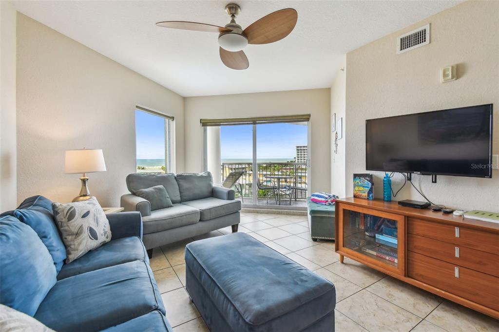 A balcony with a glass table and lounge chair overlooks a coastal view at sunset — 11605 GULF BOULEVARD UNIT 506, TREASURE ISLAND, FL