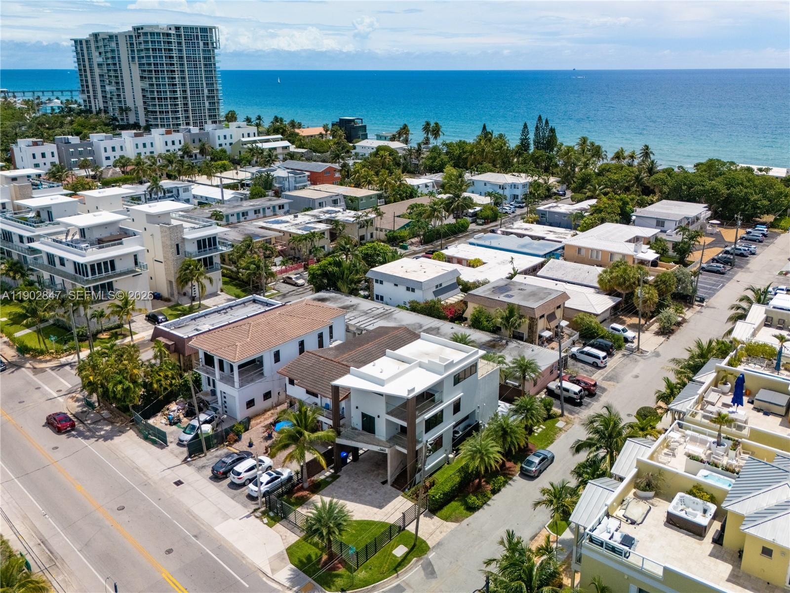 An aerial view shows a modern multi-story house near a beach with surrounding residential buildings — 5601 N Ocean Dr, Hollywood FL 33019, HOLLYWOOD, FL