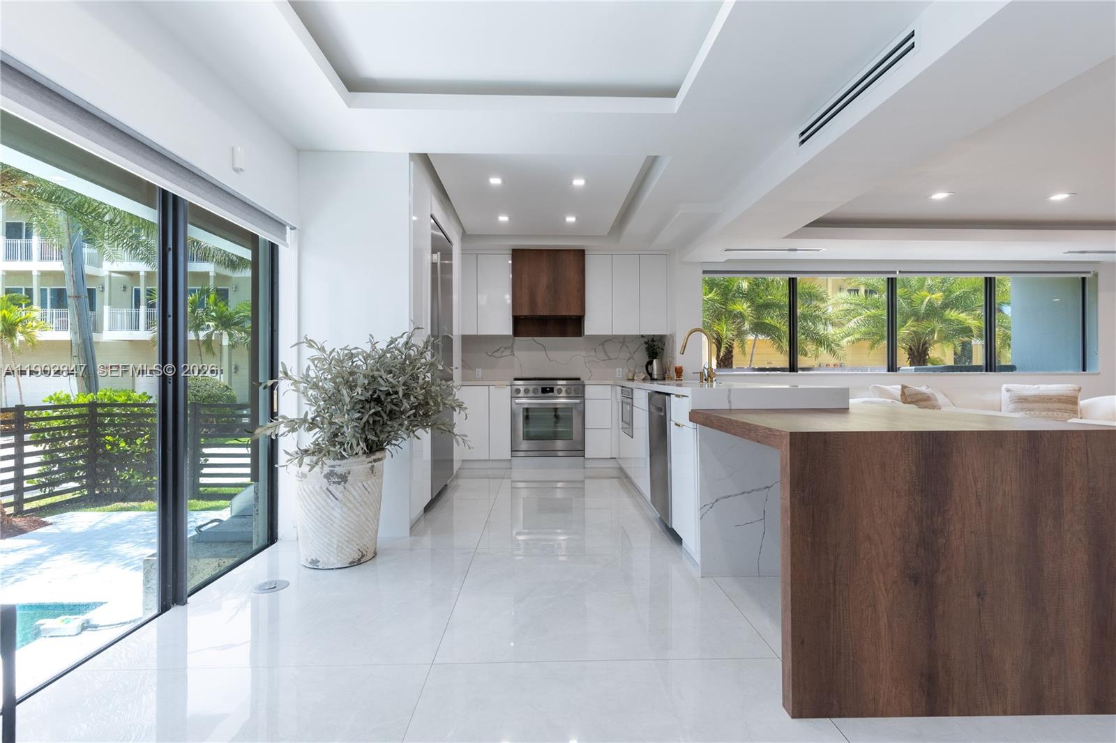 A modern kitchen features white cabinetry, a wood-accented range hood, and a waterfall island — 5601 N Ocean Dr, Hollywood FL 33019, HOLLYWOOD, FL