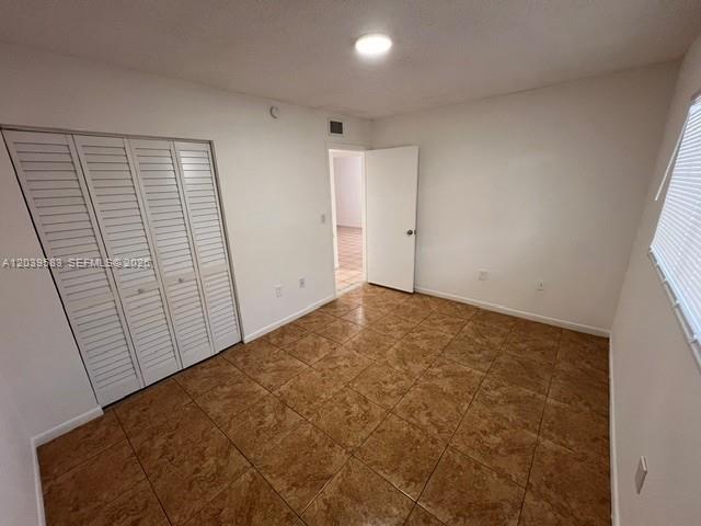 An empty room features white walls, a louvered closet, and brown tiled flooring — 2690 W 76th St # 106, Hialeah FL 33016, HIALEAH, FL