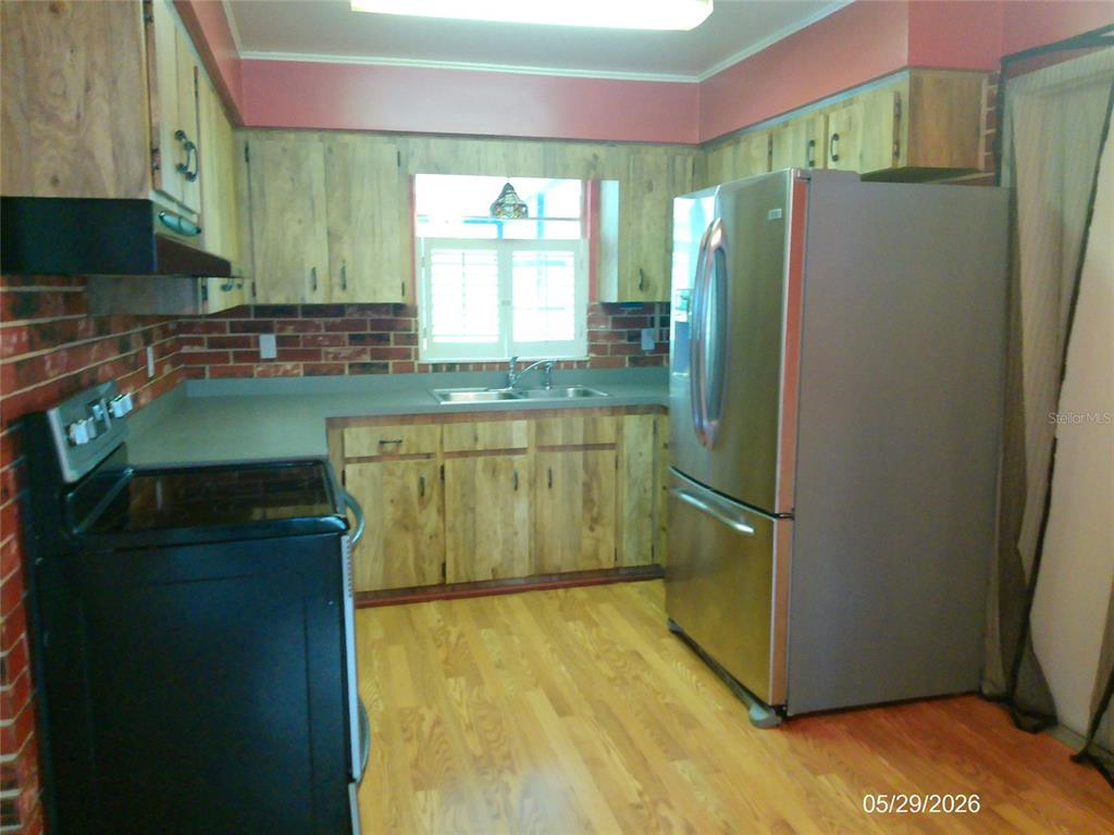 A kitchen features wood-grain cabinets, a stainless steel refrigerator, a black stove, and brick accents — 6131 DOE CIRCLE E, LAKELAND, FL