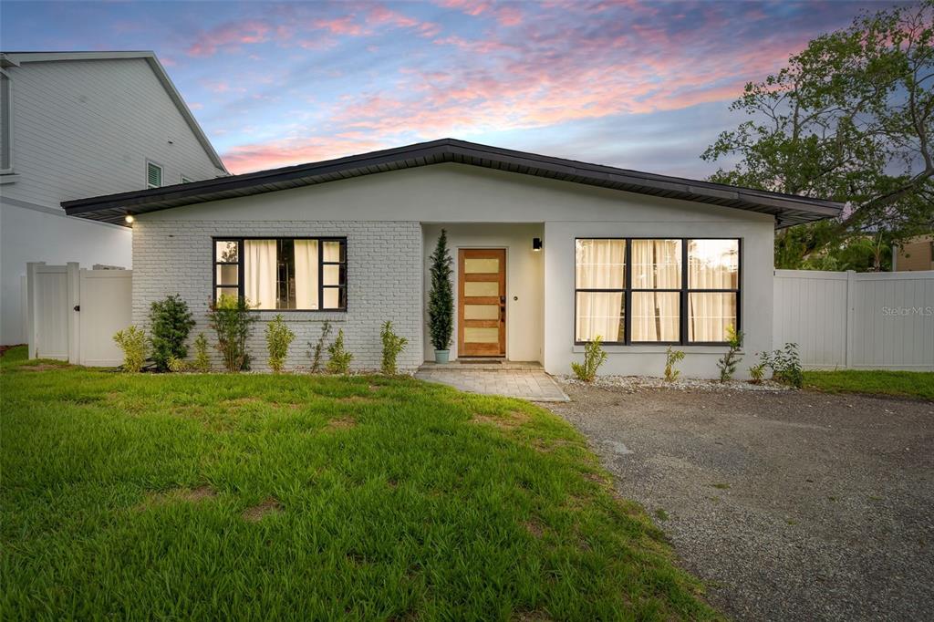 A single-story house with a white brick facade, a wooden front door, and a gravel driveway — 3601 W DALE AVENUE, TAMPA, FL