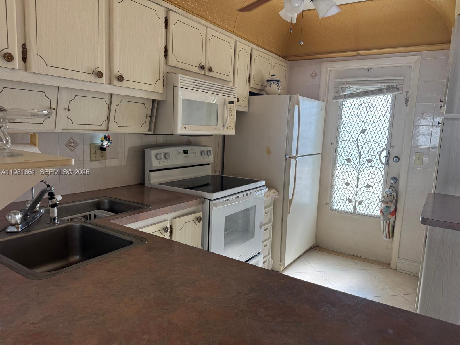 A kitchen features white cabinetry, a white stove and refrigerator, and a dark countertop — 450 Paradise Isle Blvd # 209, Hallandale Beach FL 33009, HALLANDALE BEACH, FL