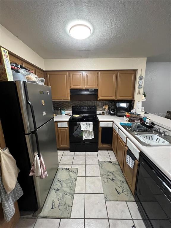 A kitchen features wood cabinets, black appliances, a stainless steel refrigerator, and tiled flooring — 13941 FAIRWAY ISLAND DRIVE UNIT 733, ORLANDO, FL