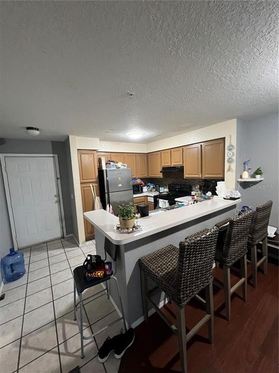 A kitchen features brown cabinets, a breakfast bar with wicker stools, and tiled flooring — 13941 FAIRWAY ISLAND DRIVE UNIT 733, ORLANDO, FL