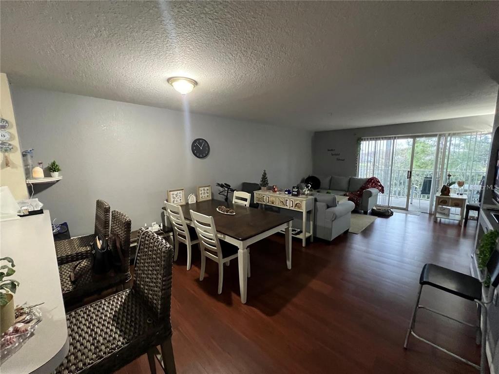 An open-concept living and dining area features wood-look flooring, a dining table, and sliding doors — 13941 FAIRWAY ISLAND DRIVE UNIT 733, ORLANDO, FL