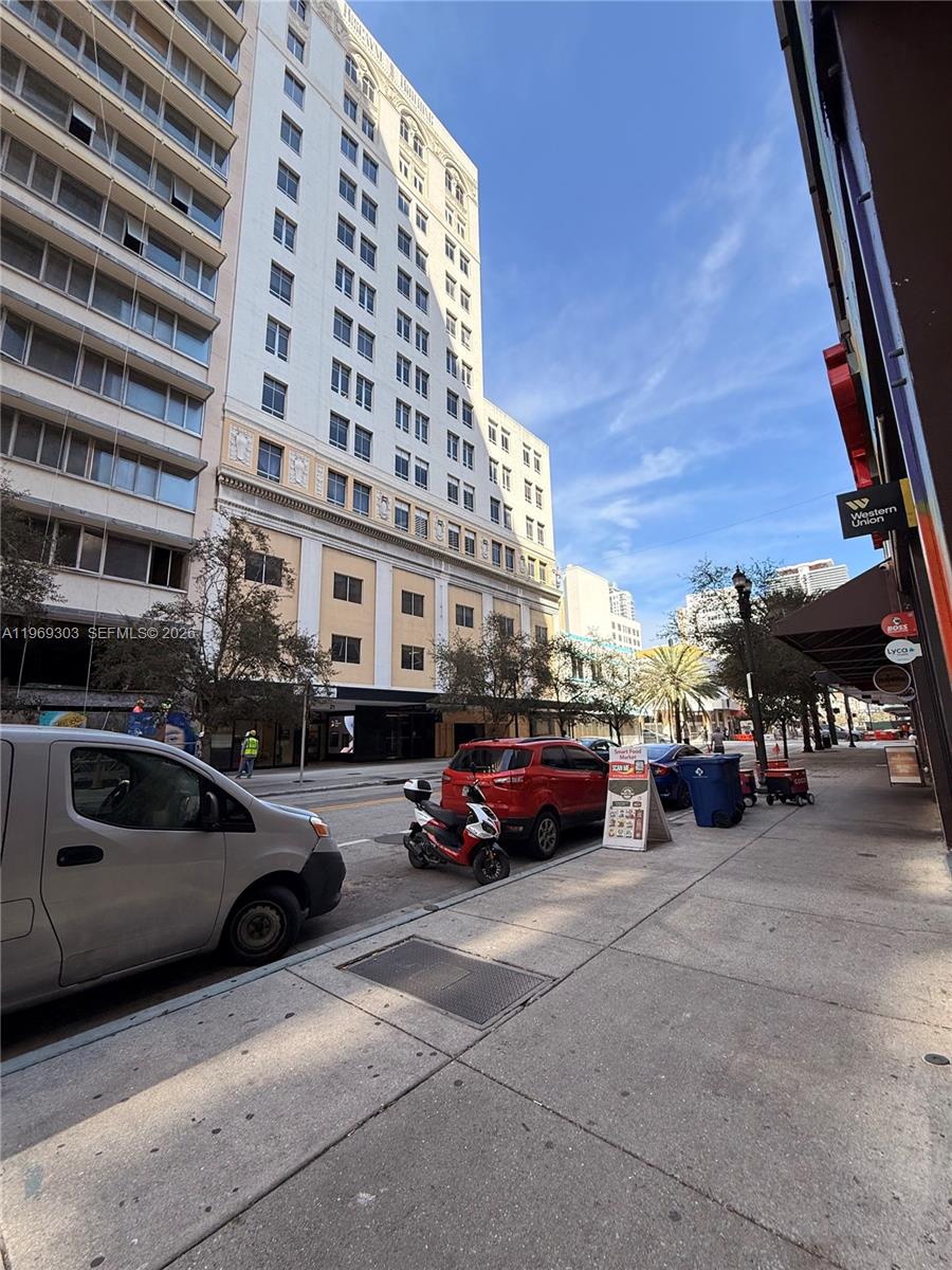 A street-level view shows a white high-rise building, parked vehicles, and a sidewalk — 28 W Flagler St # 102, Miami FL 33130, MIAMI, FL