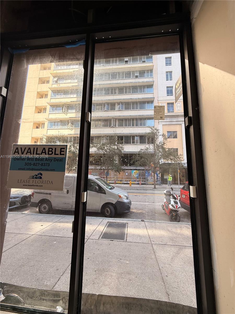 A view through a glass storefront window looking out onto a city street with buildings — 28 W Flagler St # 102, Miami FL 33130, MIAMI, FL