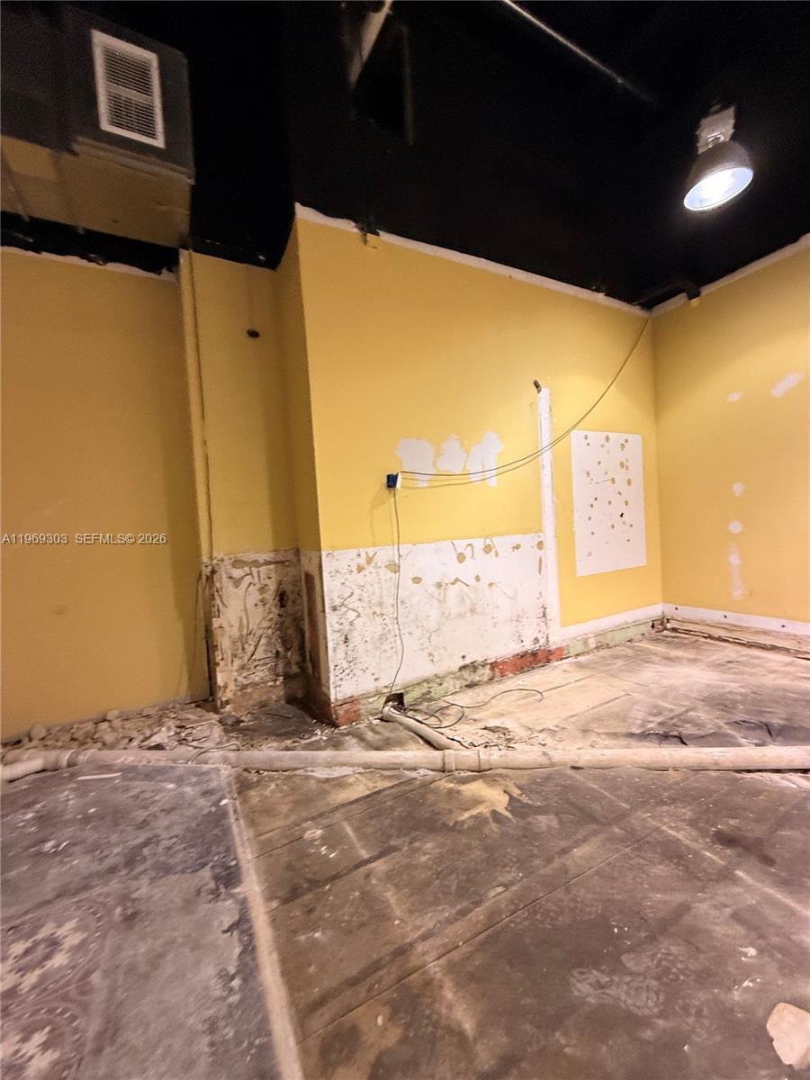 An unfinished room features yellow walls, exposed concrete flooring, and a black ceiling — 28 W Flagler St # 102, Miami FL 33130, MIAMI, FL