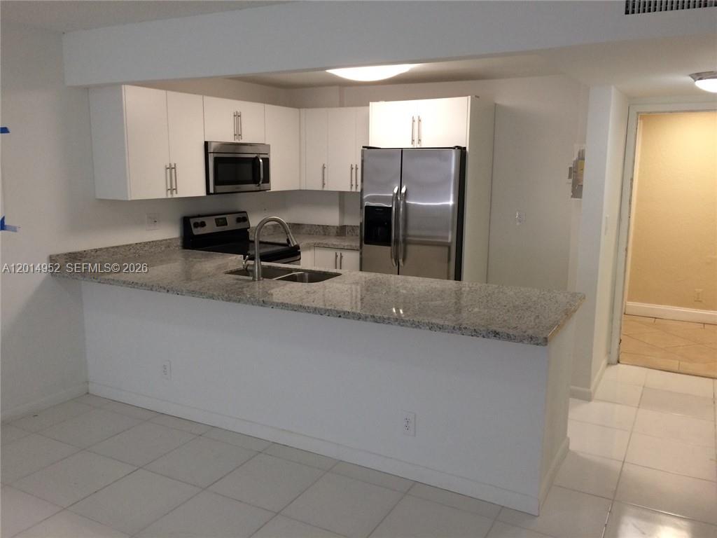 A kitchen features white cabinets, stainless steel appliances, and a granite-topped breakfast bar — 9143 SW 77 AV # B107, Miami FL 33156, MIAMI, FL