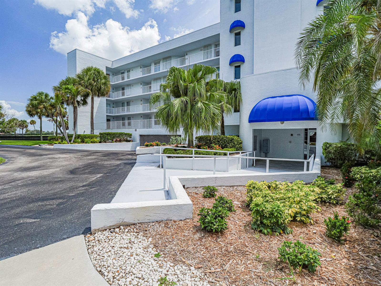 A multi-story white apartment building features blue awnings, balconies, and a landscaped entrance ramp — 6005 River Run Drive, Sebastian FL 32958, SEBASTIAN, FL