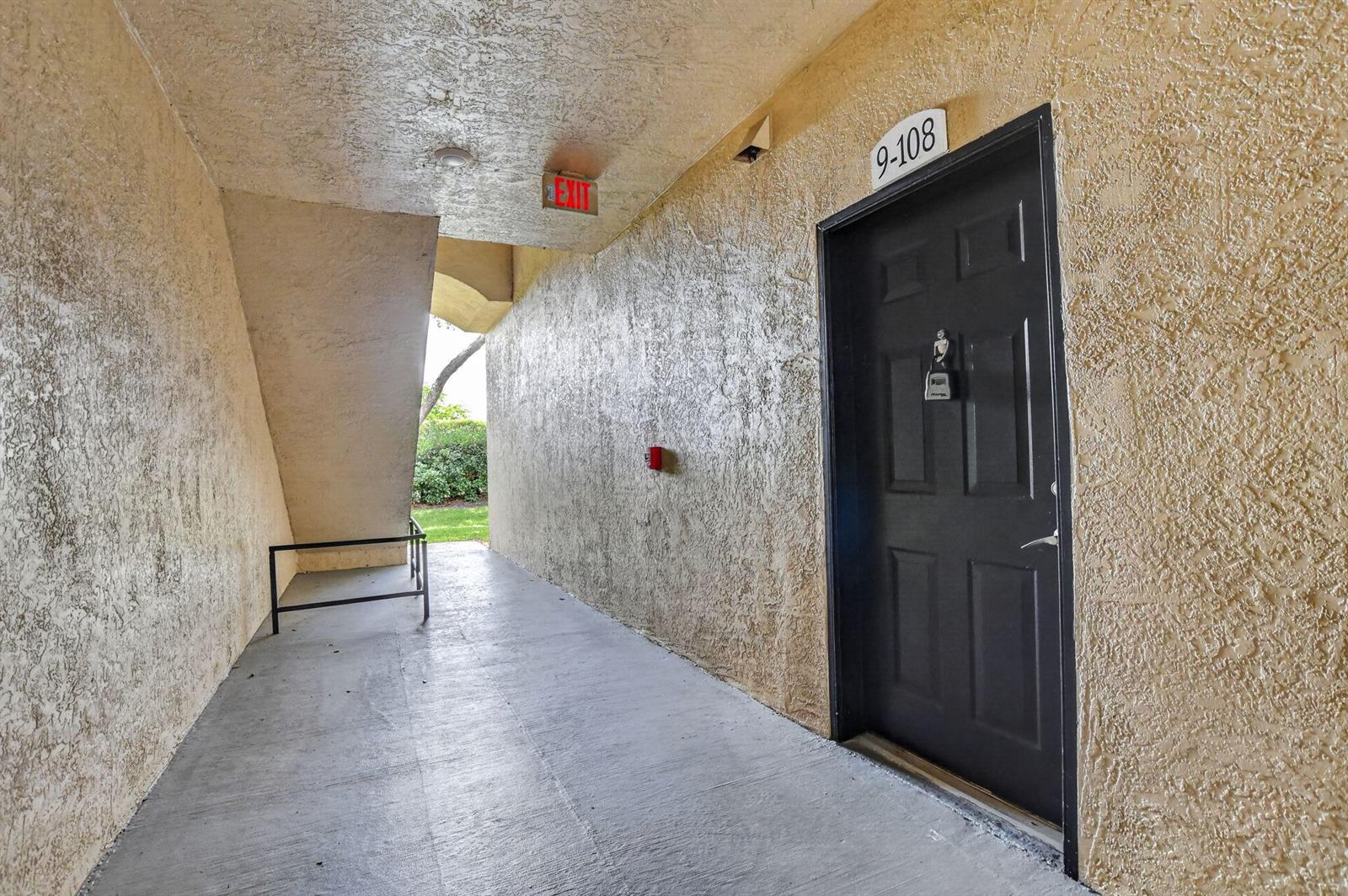 A dark door labeled 9-108 is set into a textured beige wall along a walkway — 15085 Michelangelo Boulevard # 108, Delray Beach FL 33446, DELRAY BEACH, FL
