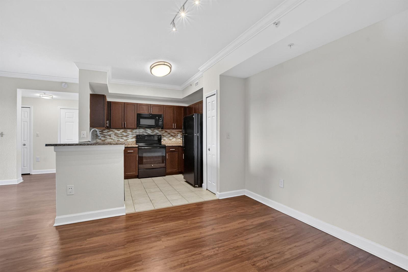 A kitchen with dark wood cabinets, black appliances, and tile flooring opens to a living area — 15085 Michelangelo Boulevard # 108, Delray Beach FL 33446, DELRAY BEACH, FL
