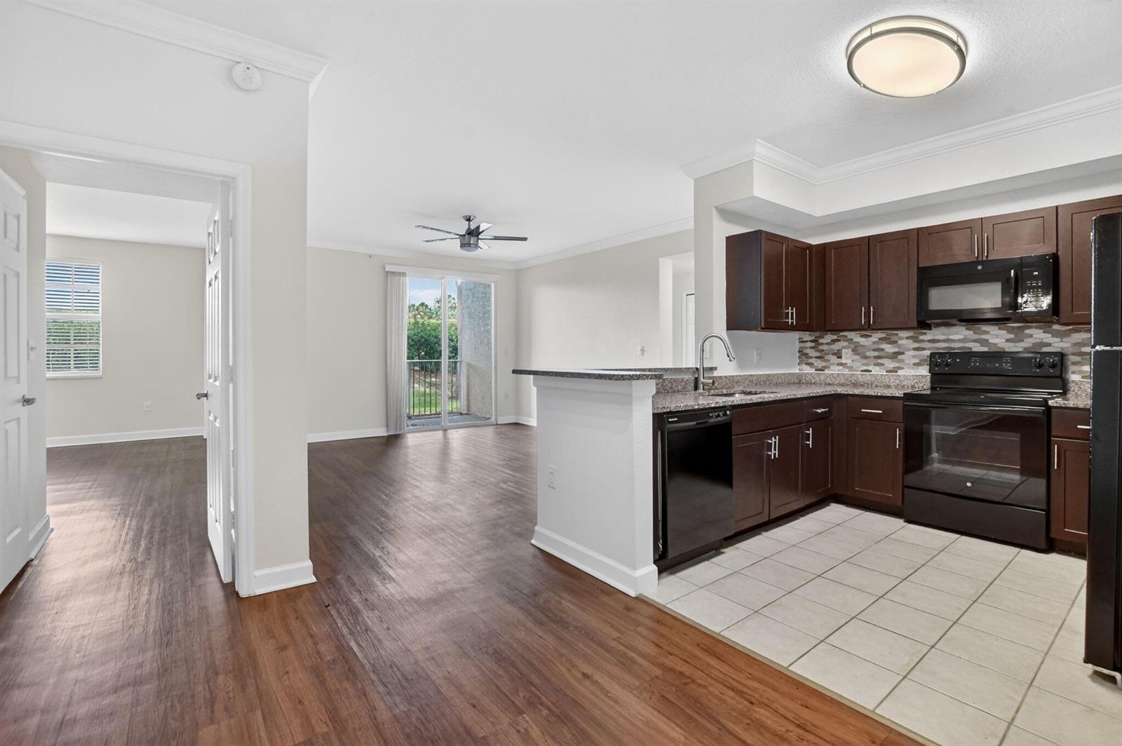An open-concept kitchen with dark wood cabinets and tile flooring overlooks a wood-floored living area — 15085 Michelangelo Boulevard # 108, Delray Beach FL 33446, DELRAY BEACH, FL