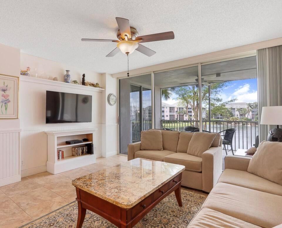 A living room features a beige sofa, granite coffee table, wall-mounted television, and balcony view — 353 S Us Highway 1 # A207, Jupiter FL 33477, JUPITER, FL