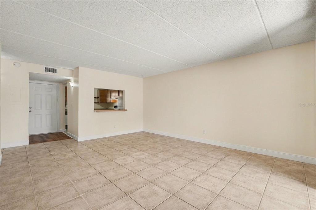 An empty room features beige tiled flooring, light-colored walls, and a kitchen pass-through window — 2845 SOMERSET PARK DRIVE UNIT 101, TAMPA, FL