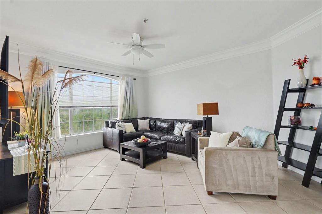 A living room features a black sectional sofa, a beige armchair, and a ladder bookshelf — 4306 BAYSIDE VILLAGE DRIVE UNIT 301, TAMPA, FL