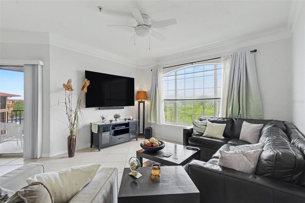 A living room features a black leather sectional, a wall-mounted television, and a large window — 4306 BAYSIDE VILLAGE DRIVE UNIT 301, TAMPA, FL