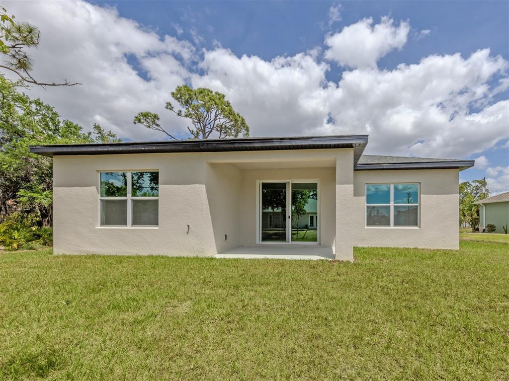 The rear exterior of a single-story house features a covered patio and sliding glass doors — 1047 COMFORT LANE, NORTH PORT, FL