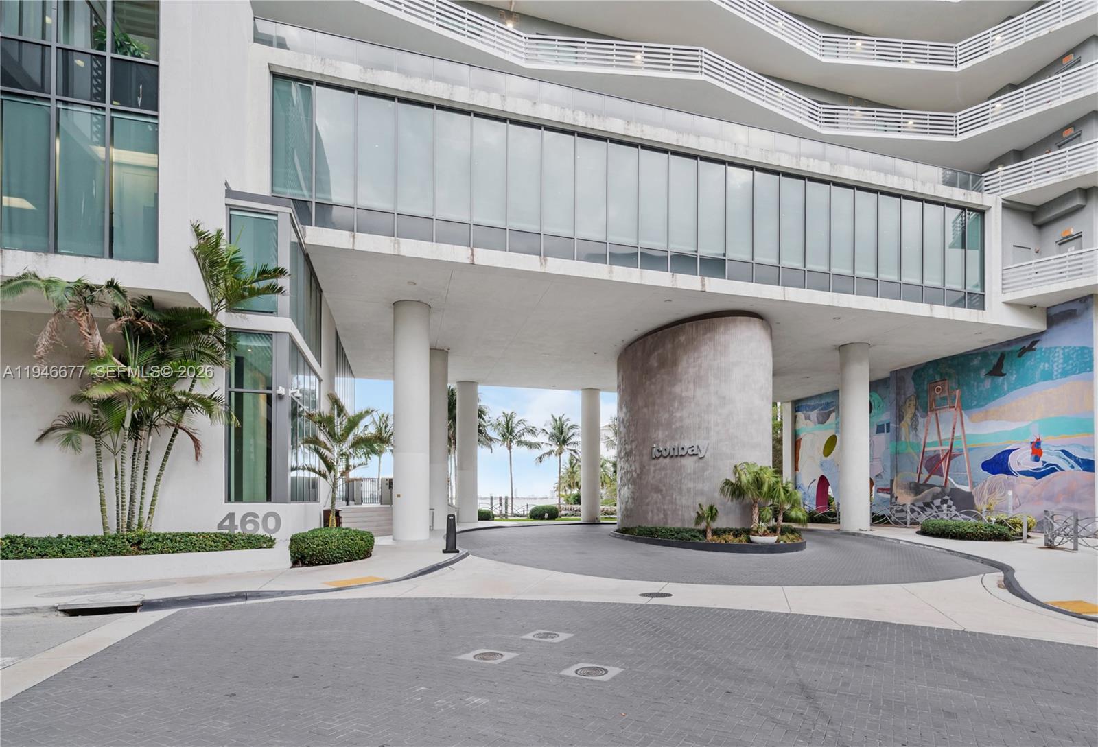 The exterior entrance of a modern building features a circular driveway, concrete columns, and murals — 460 NE 28th St # 3002, Miami FL 33137, MIAMI, FL