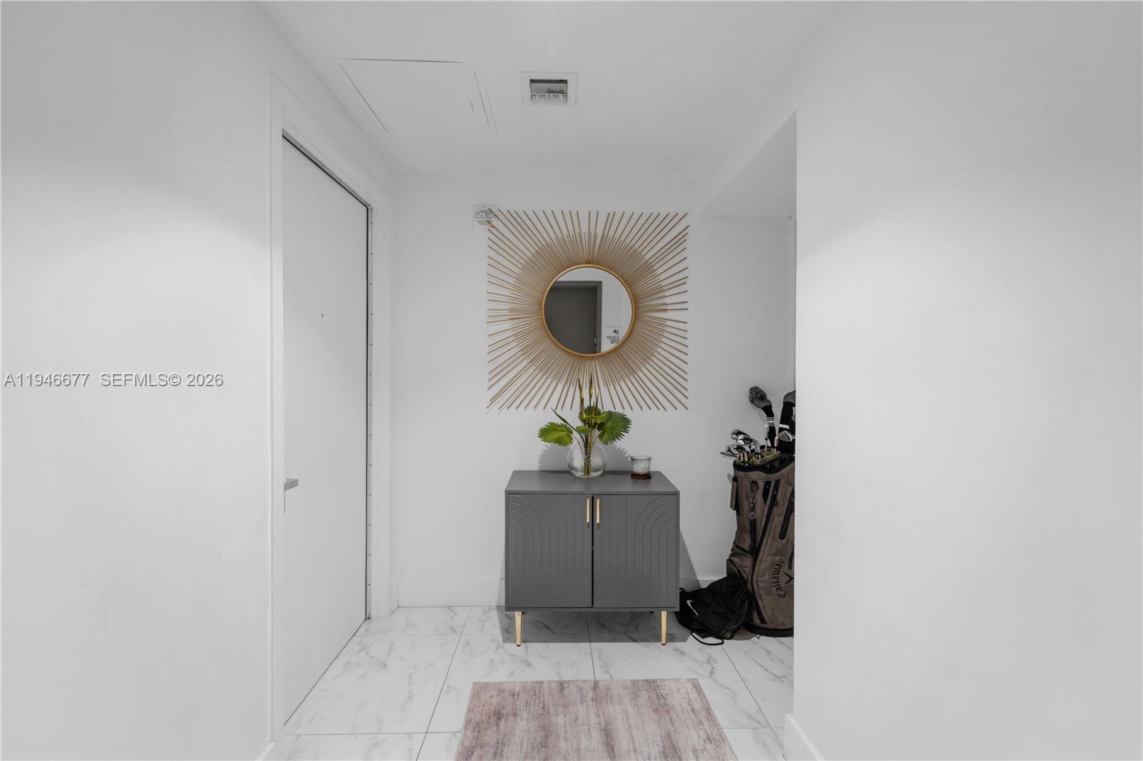 A white-walled entryway features a gray cabinet, a sunburst mirror, and a golf bag — 460 NE 28th St # 3002, Miami FL 33137, MIAMI, FL