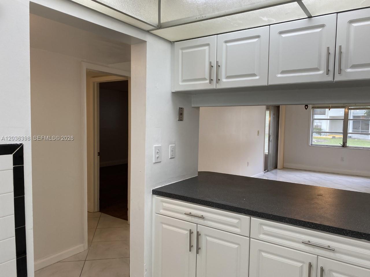 A kitchen features white cabinets, a dark countertop, and a pass-through window to another room — 6507 Winfield Blvd # C, Margate FL 33063, MARGATE, FL