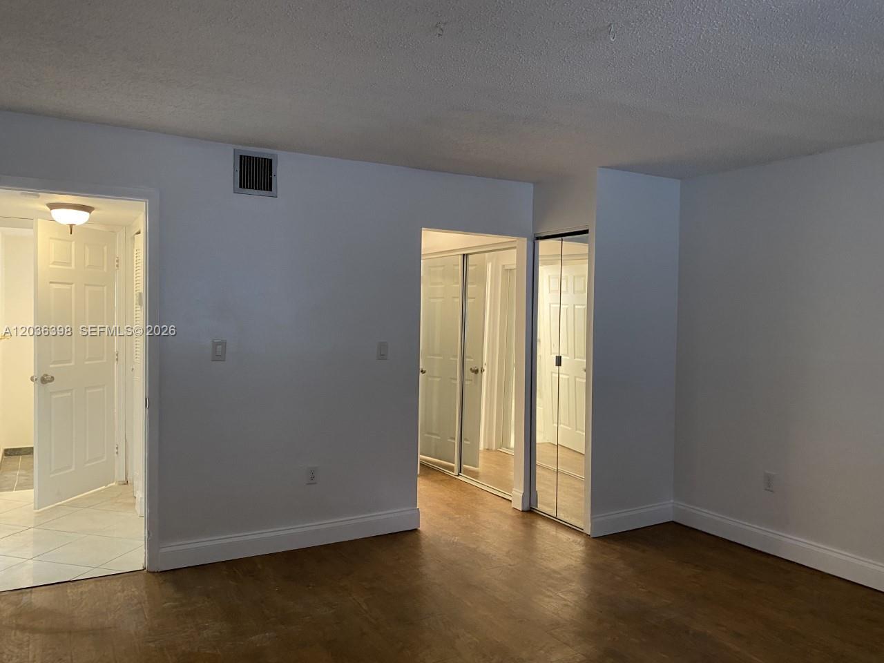 A room with wood-look flooring, white walls, and mirrored closet doors leading to a hallway — 6507 Winfield Blvd # C, Margate FL 33063, MARGATE, FL