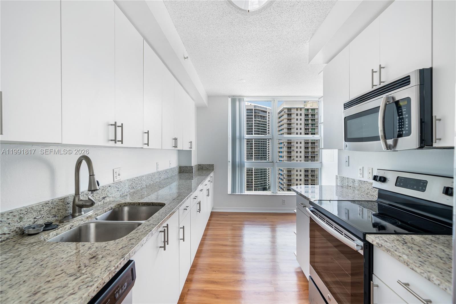 A galley kitchen features white cabinets, granite countertops, stainless steel appliances, and a window view — 1111 Brickell Bay Dr # 3108, Miami FL 33131, MIAMI, FL