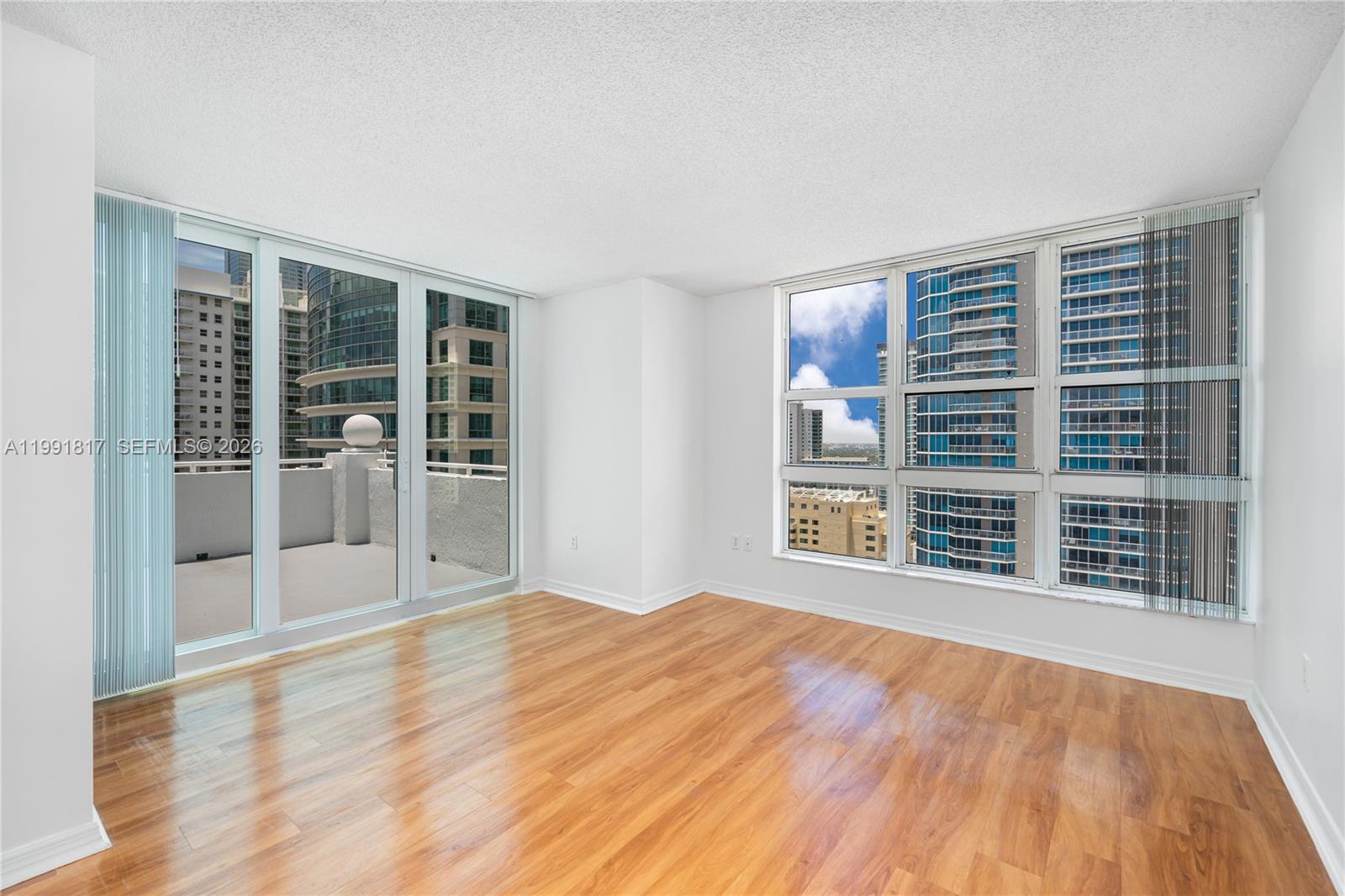 An empty room features light wood flooring, white walls, large windows, and a glass balcony door — 1111 Brickell Bay Dr # 3108, Miami FL 33131, MIAMI, FL