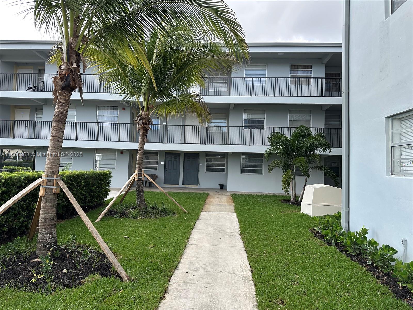 A three-story apartment building features exterior walkways, palm trees, and a concrete path — 1100 NE 1 # 111, Hallandale Beach FL 33009, HALLANDALE BEACH, FL