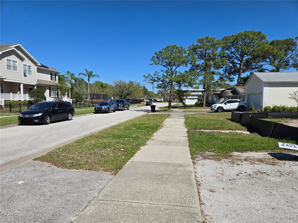 A suburban street scene features a sidewalk, parked cars, and residential houses under a clear sky — 134 49TH AVENUE N, ST PETERSBURG, FL