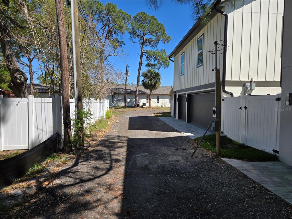 A gravel alleyway runs between a white vinyl fence and the side of a house — 134 49TH AVENUE N, ST PETERSBURG, FL