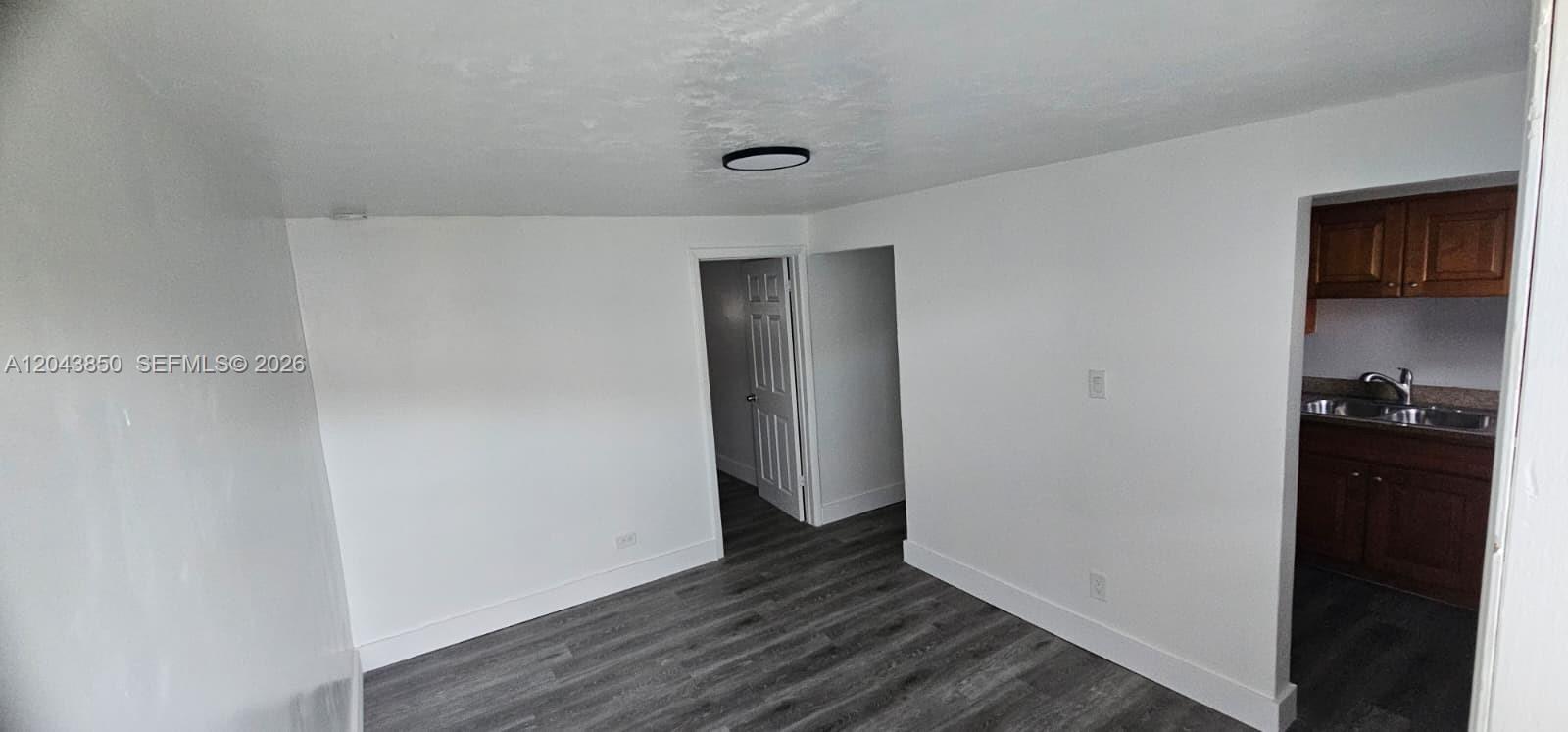 A room with gray wood-look flooring, white walls, a ceiling light, and an adjacent kitchen — WEST PARK, FL