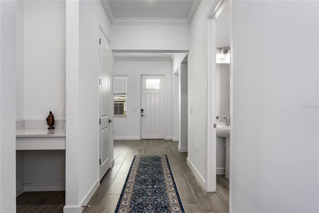 A hallway with wood-look tile flooring leads to an exterior door and a small bathroom — 17439 HOLLY WELL AVENUE, WIMAUMA, FL