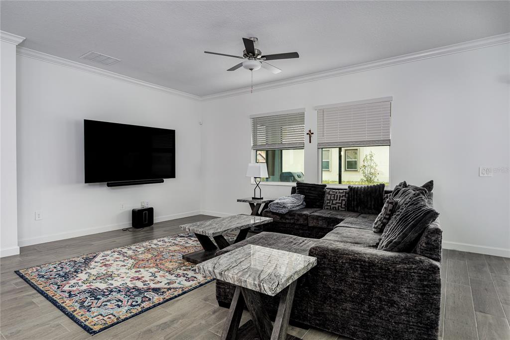 A living room features a large sectional sofa, a wall-mounted television, and gray tile flooring — 17439 HOLLY WELL AVENUE, WIMAUMA, FL