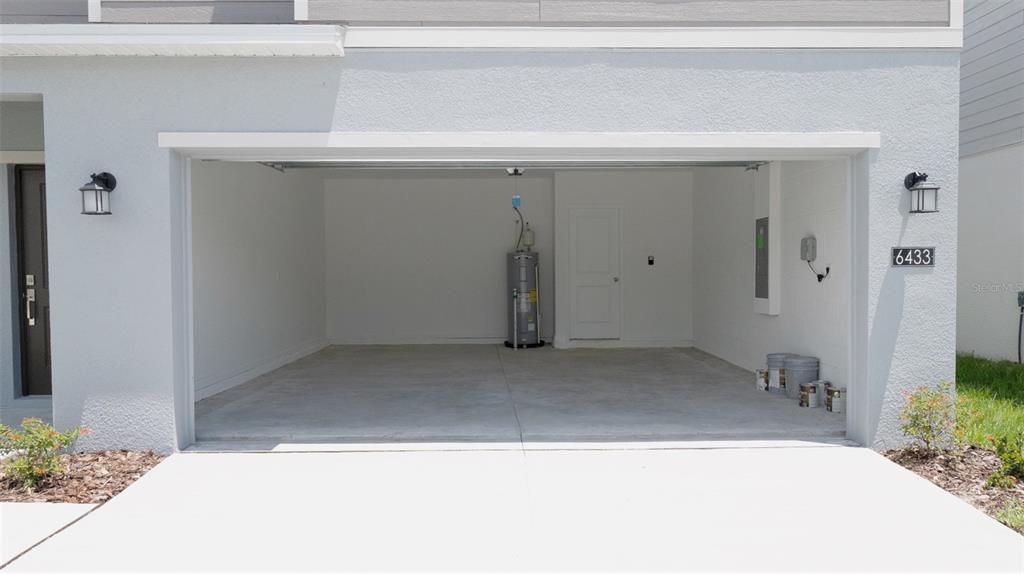 An open garage features a concrete floor, a water heater, and a white interior door — 6433 DOMIZIO DRIVE, WINTER HAVEN, FL