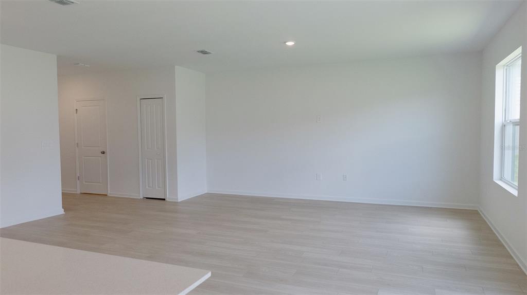 An empty living room features light wood-look flooring, white walls, and a single window — 6433 DOMIZIO DRIVE, WINTER HAVEN, FL