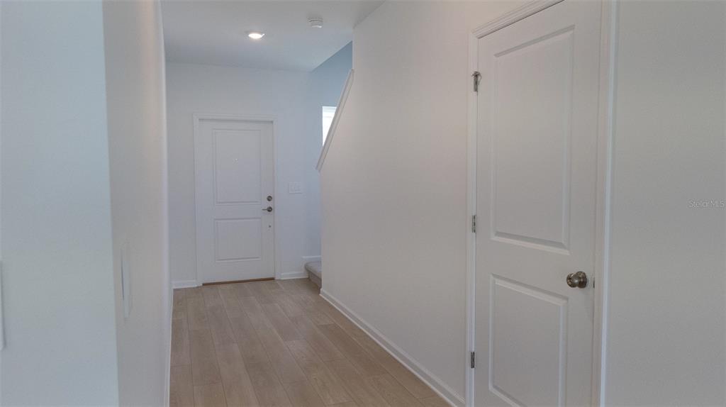 A hallway features light wood-look flooring, white walls, and two white interior doors — 6433 DOMIZIO DRIVE, WINTER HAVEN, FL