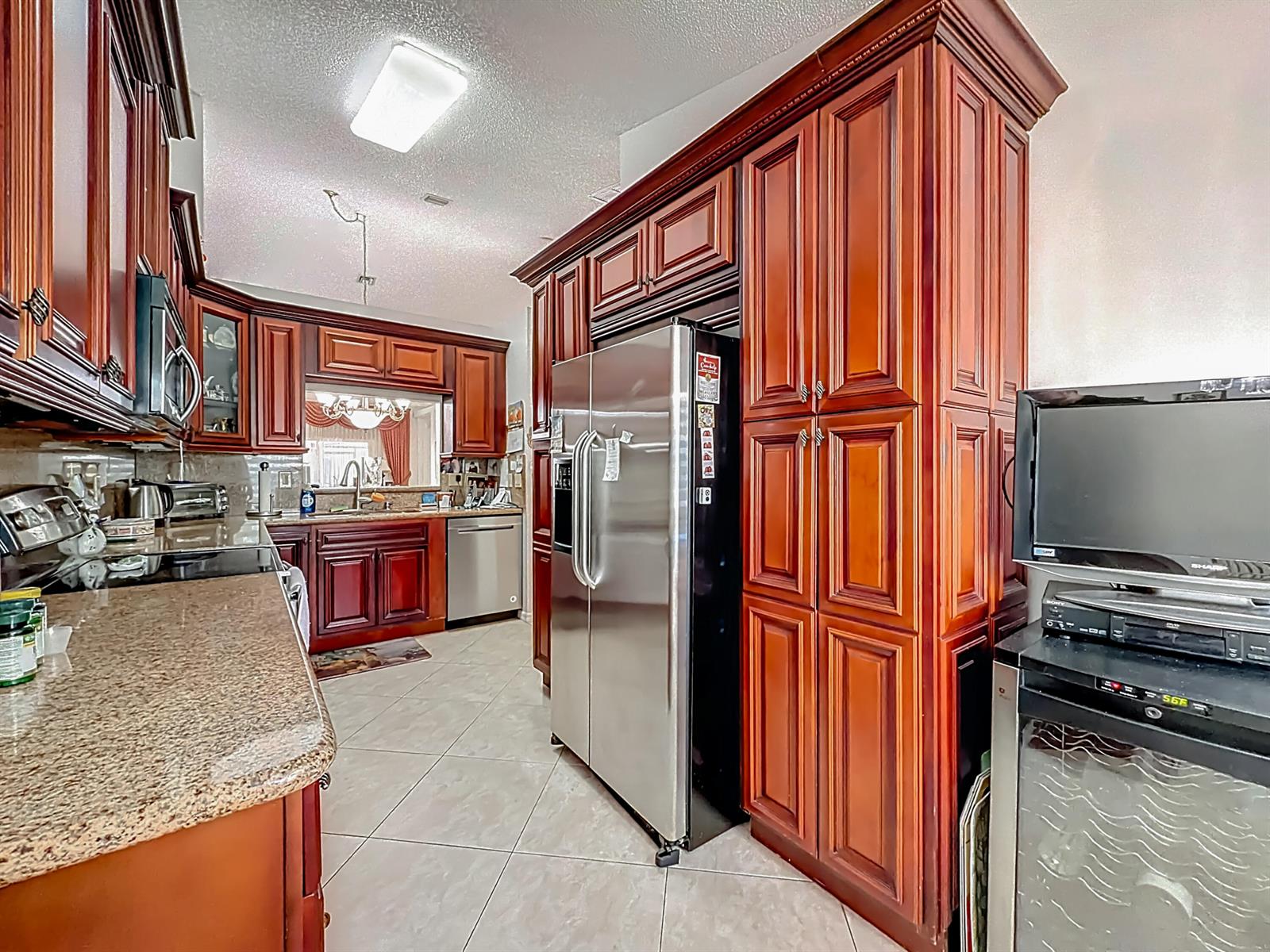 A kitchen features dark wood cabinets, stainless steel appliances, granite countertops, and tile flooring — 6174 Caladium Road, Delray Beach FL 33484, DELRAY BEACH, FL