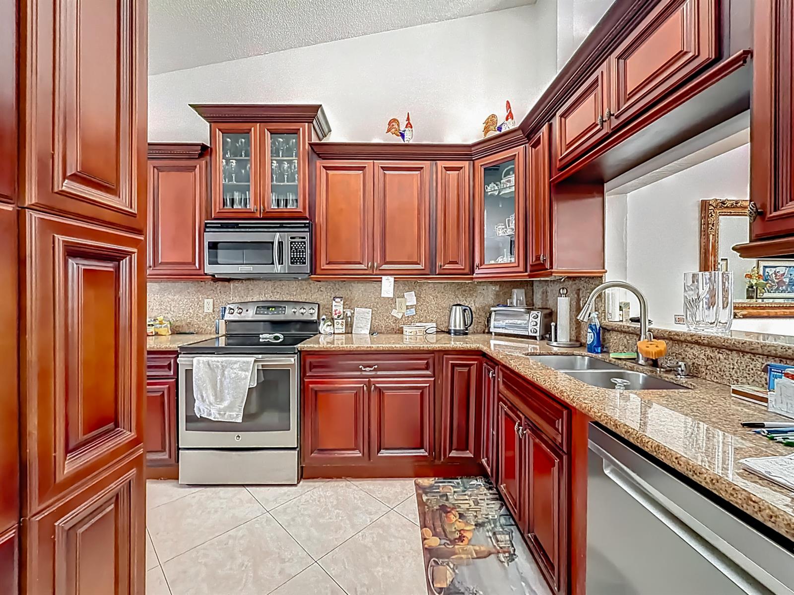 A kitchen features dark wood cabinets, granite countertops, stainless steel appliances, and tile flooring — 6174 Caladium Road, Delray Beach FL 33484, DELRAY BEACH, FL