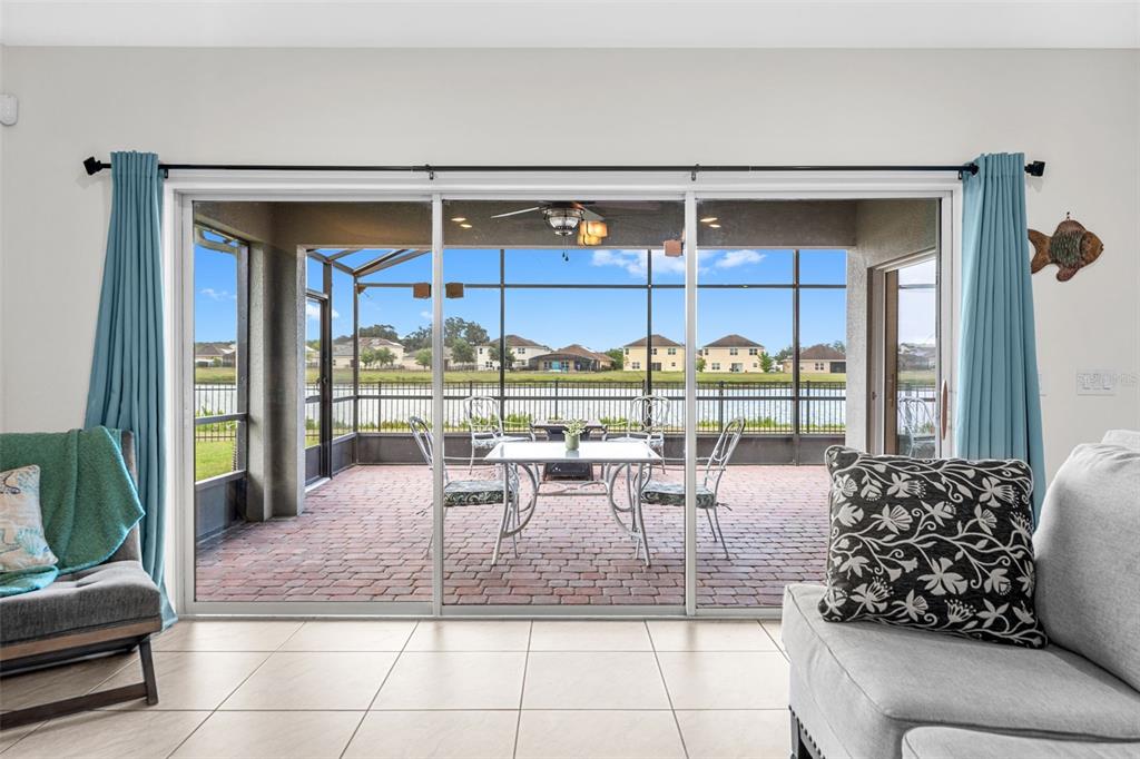 A living room with tile floors looks out through sliding glass doors to a screened patio — 4851 PEARL LAKE COURT, KISSIMMEE, FL