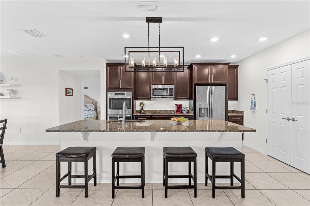 A kitchen features dark wood cabinets, granite countertops, a large island, and four bar stools — 4851 PEARL LAKE COURT, KISSIMMEE, FL