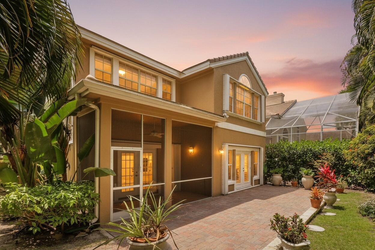 A two-story house exterior with a screened-in porch, brick patio, and lush landscaping at sunset — 12 Grand Bay Circle, Juno Beach FL 33408, JUNO BEACH, FL