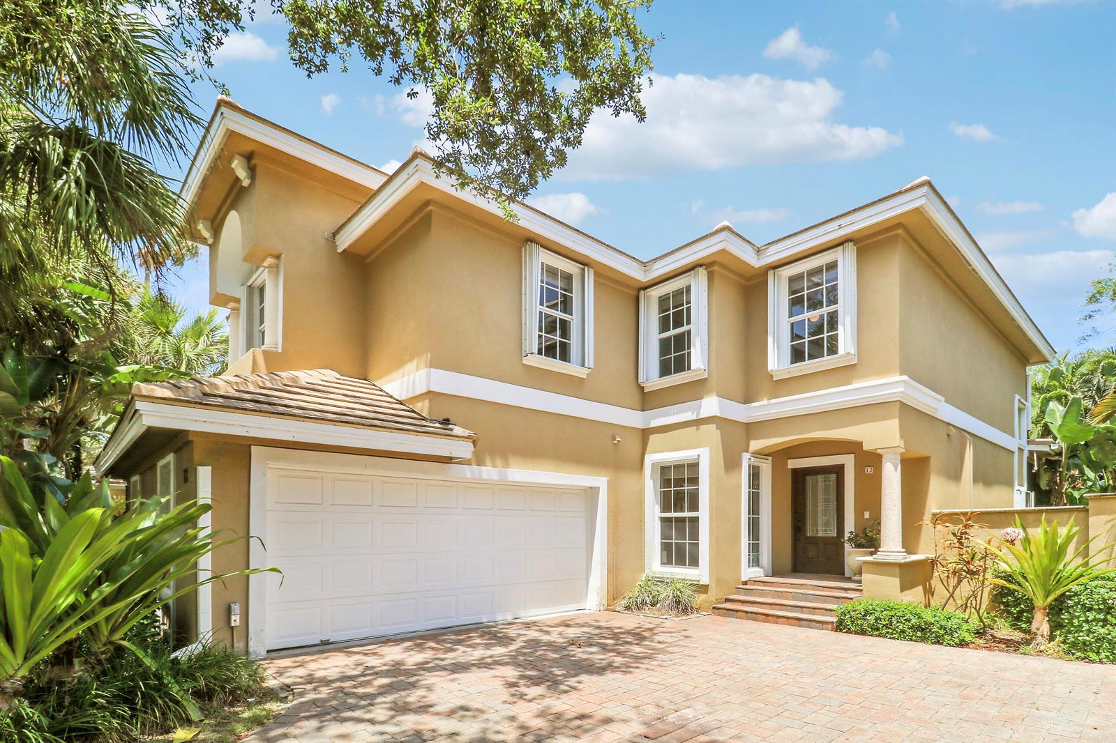 A two-story tan stucco house features a two-car garage and a brick paver driveway — 12 Grand Bay Circle, Juno Beach FL 33408, JUNO BEACH, FL