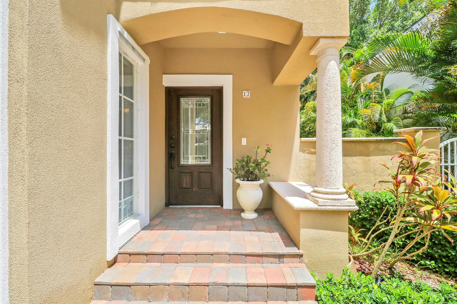 A tan stucco home entrance features a brown front door, stone steps, and a column — 12 Grand Bay Circle, Juno Beach FL 33408, JUNO BEACH, FL