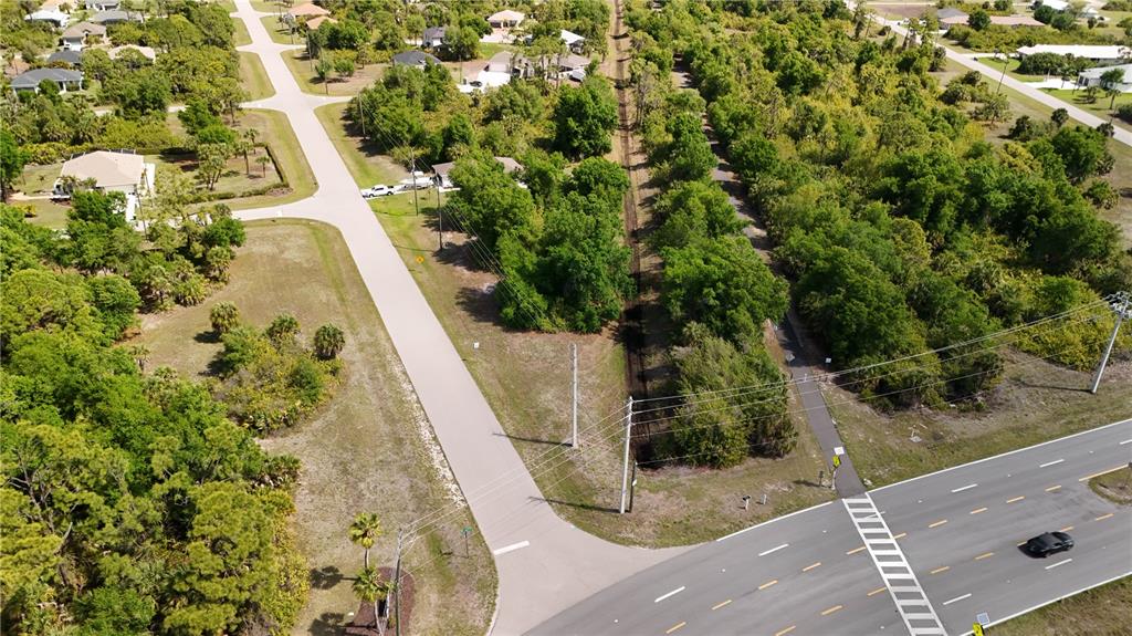 An aerial view shows a paved road intersecting a multi-lane highway near wooded land — 103 ANTILLA DRIVE, ROTONDA WEST, FL