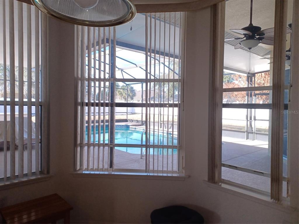 A dining area with vertical blinds overlooks a screened-in patio and a swimming pool — 3513 BEAU CHENE DRIVE, KISSIMMEE, FL